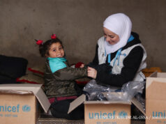 (Right) A UNICEF worker helps a young girl open up a box of winter supplies in Ghernata village in northern rural Aleppo in the Syrian Arab Republic on 29 December 2020. Years of violence, displacement and loss of livelihoods have taken a toll on families across Syria who are left unable to provide for their children’s most basic needs, including for warm clothes to fend off the cold winter. Their vulnerability is compounded by their rudimentary living conditions, with many having been forced to flee their homes with nothing but the clothes on their back, while others returned to their damaged houses following a lull in violence, amid a severe lack of services. To help ease the financial burden on families, and thanks to a generous contribution by Canada and the Department for International Development (DFID), UNICEF with partners is distributing over 27,000 winter clothing kits to children aged 0-14. Each clothing kit contains a thermal outfit, a winter jacket, woolen hat, scarf and gloves, as well as winter shoes.