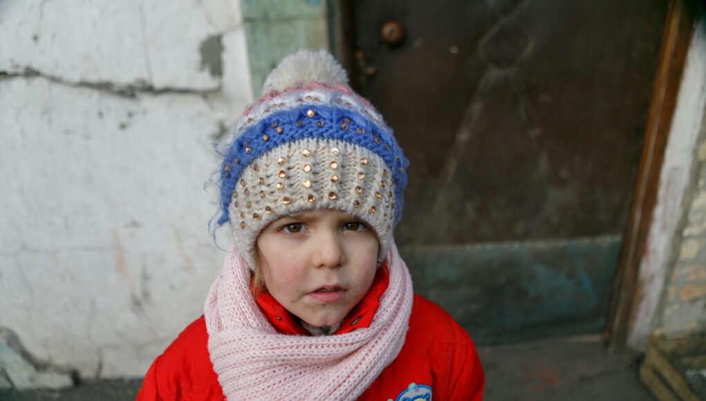 Four-year-old Vika stands by the door of her house in Krasnohorivka, Donetsk region. Vika often comes to the front yard waiting to see the snow. The girl likes sledding and to build a snowman.
